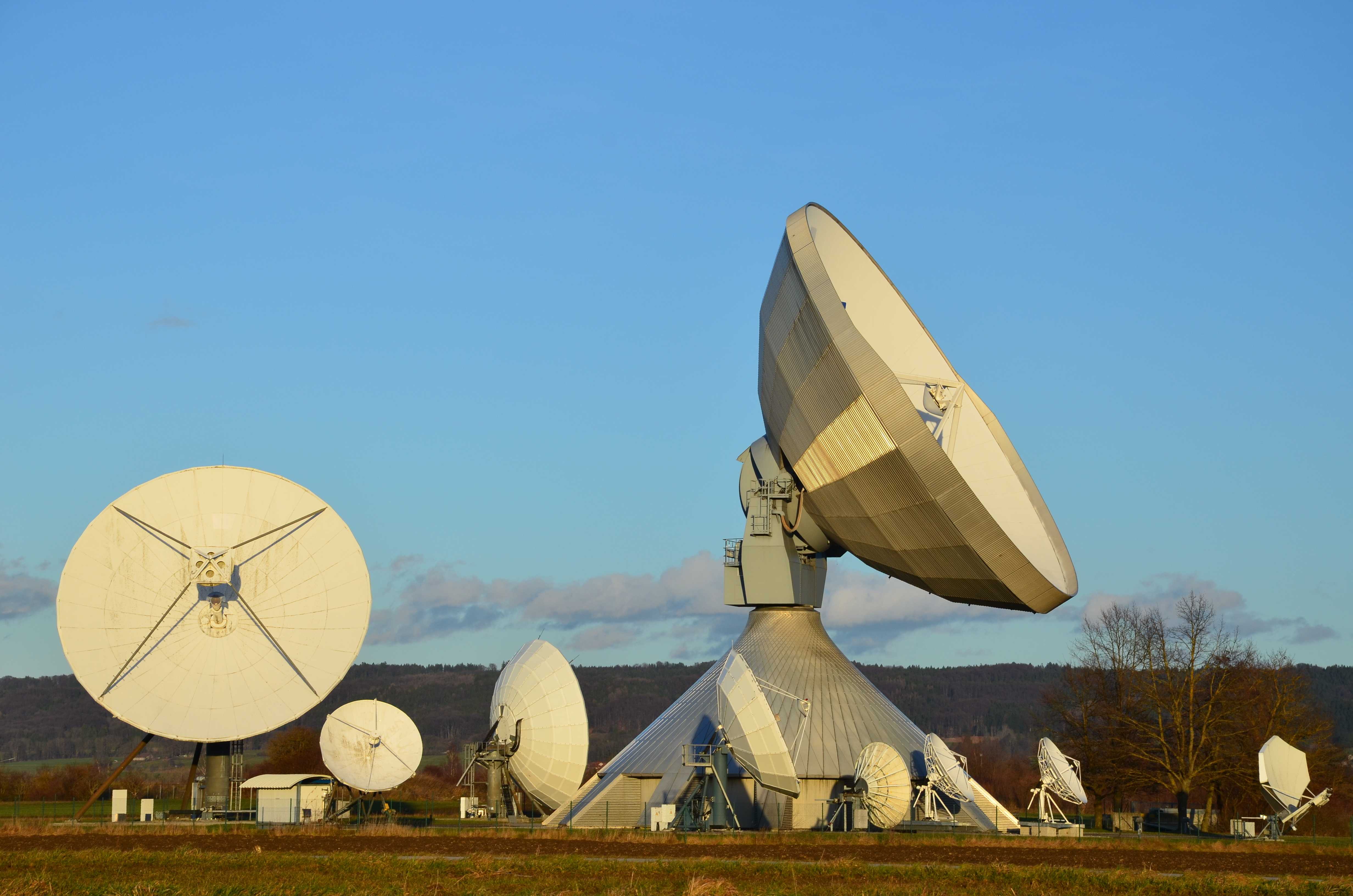 Medium sized satellite ground station with multiple antennas against a blue sky