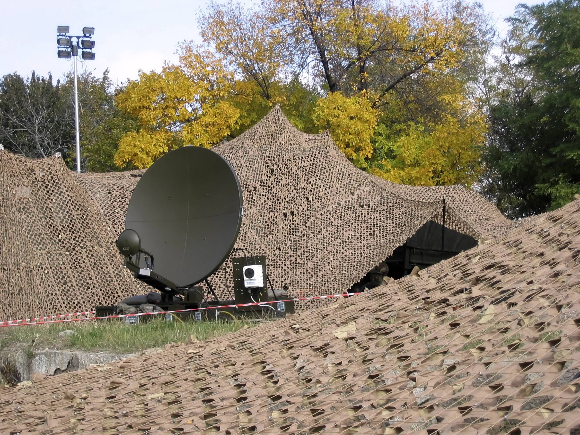 Green tactical antenna amongst brown camouflage nets in a forest